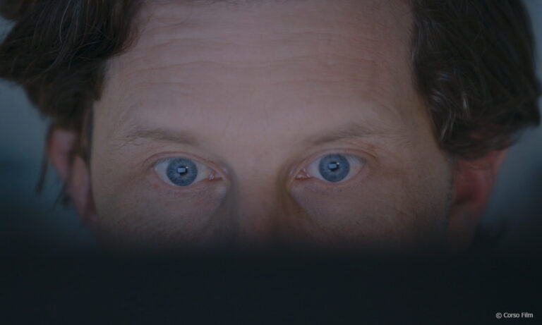 Filmstill "Auf der Spur des Geldes", zu sehen ist eine Nahaufnahme eines Gesichts. Man sieht nur die Augen, der untere Teil ist verdeckt. (c) Corso Film